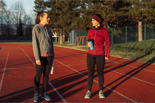 Women wearing track pants talking on a running track